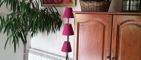 A room with a potted plant, a cabinet, a floor lamp, and a framed artwork on the wall.
