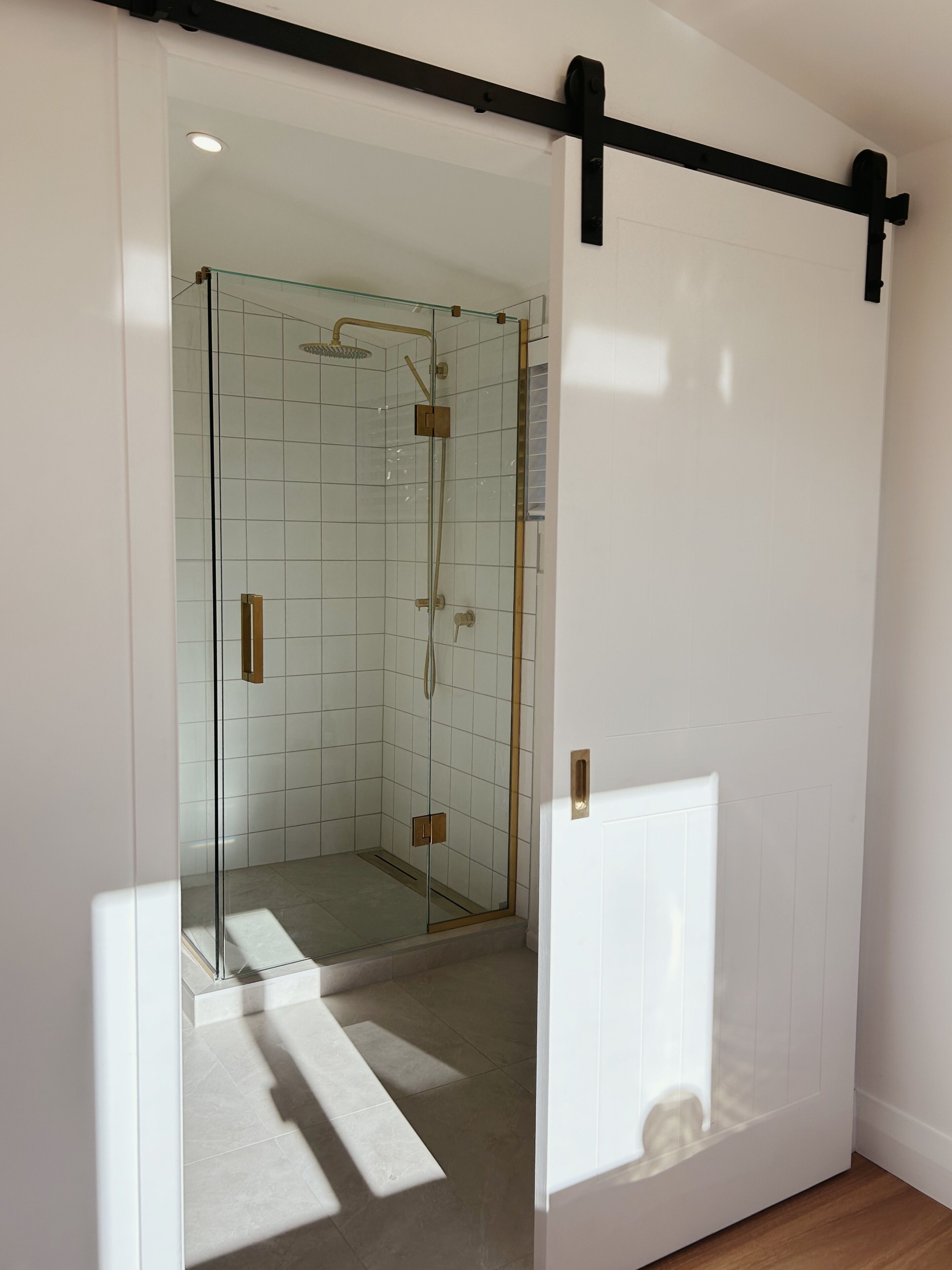 A modern bathroom with a glass shower enclosure, white tiled walls, and a black sliding door.