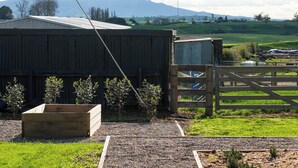 A rural farm with a wooden barn, a gravel path leading to a wooden gate, and a backdrop of mountains. - Willow View Cottage with beautiful country views - Near Waitomo (Otorohanga)
