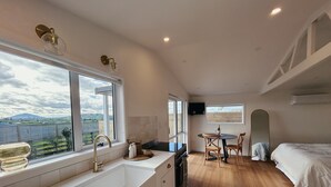 A modern kitchen with a large window, a dining area with a table and chairs, and a bedroom with a bed. - Willow View Cottage with beautiful country views - Near Waitomo (Otorohanga)