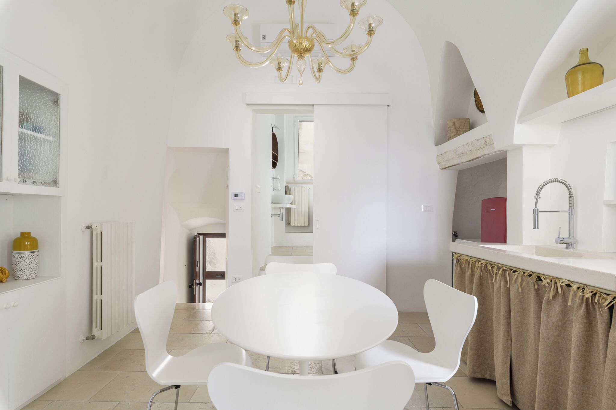 Una cocina moderna con armarios blancos, una mesa redonda para comer y una araña.