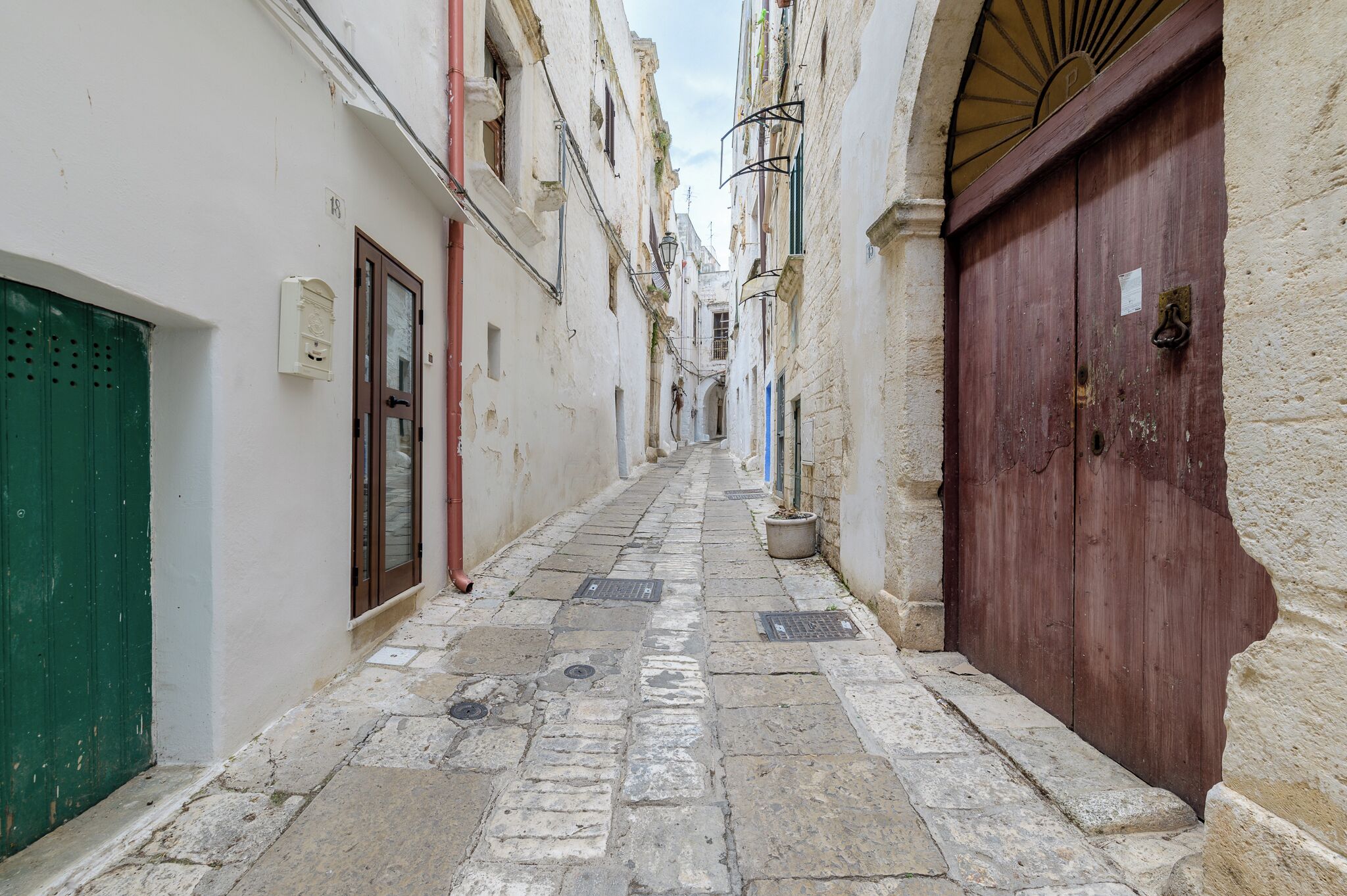 Una stretta strada acciottolata, fiancheggiata da edifici con architettura tradizionale, tra cui una porta in legno e un persiano verde.