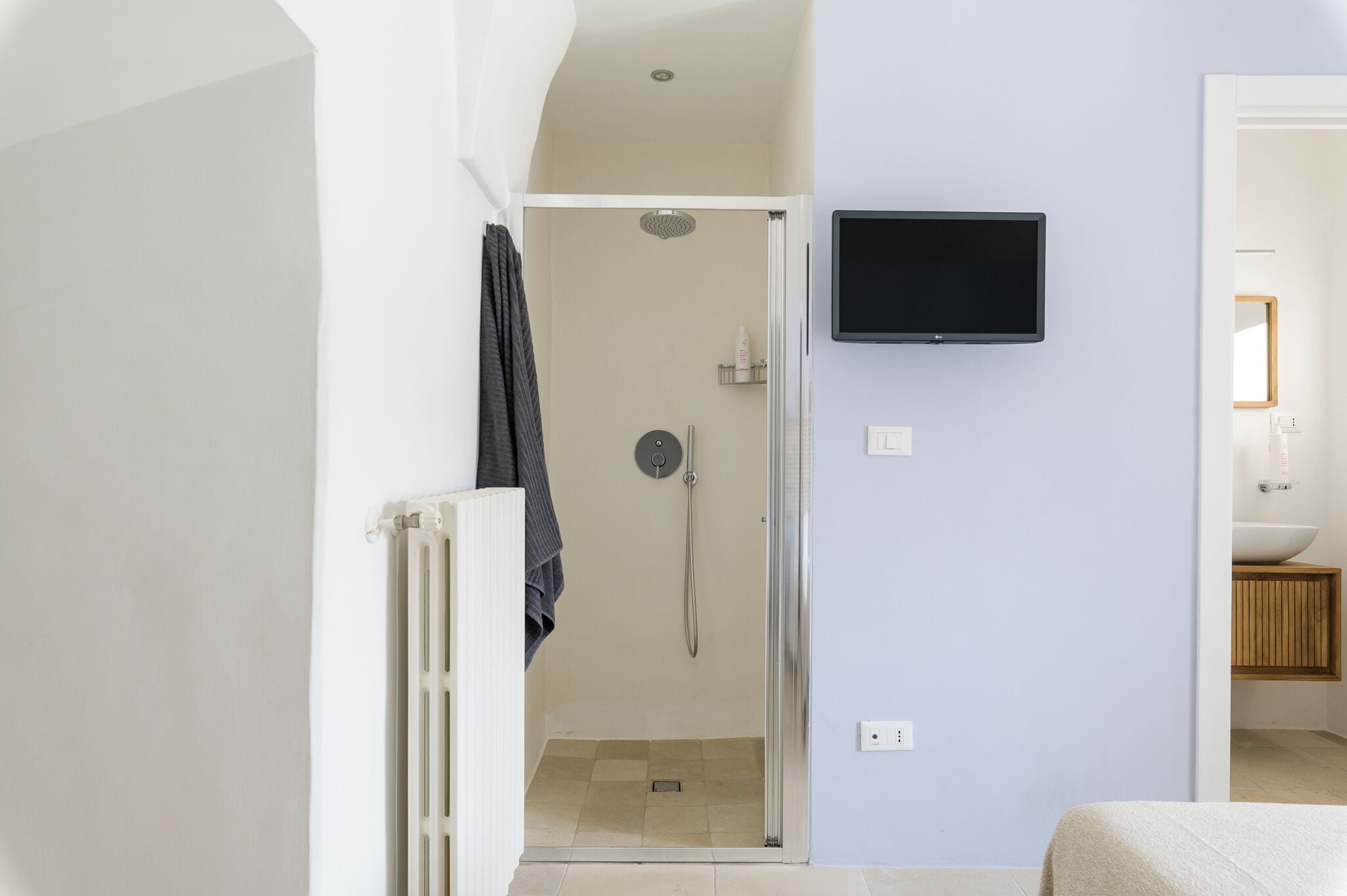 A modern bathroom with a shower, a mounted TV, and a sink with a wooden cabinet.
