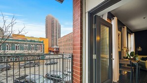 A balcony with a view of parked cars and buildings, a door with a window, and a small table with a chair. - Near Wells Fargo, King Bed and Balcony and washer dryer, fitness room, Fireplace (Des Moines)