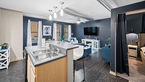 A modern kitchen with a central island, a dining area with a sofa and chairs, a flat-screen TV mounted on the wall, and a separate bedroom area with a bed and nightstand. - Near Wells Fargo, King Bed and Balcony and washer dryer, fitness room, Fireplace (Des Moines)