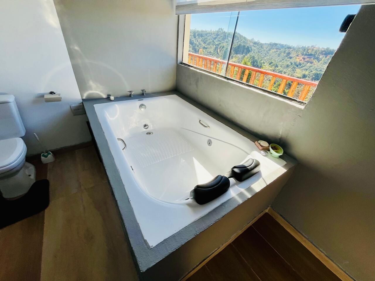 Un baño moderno con una bañera grande, un inodoro y un ventanal con vistas panorámicas.