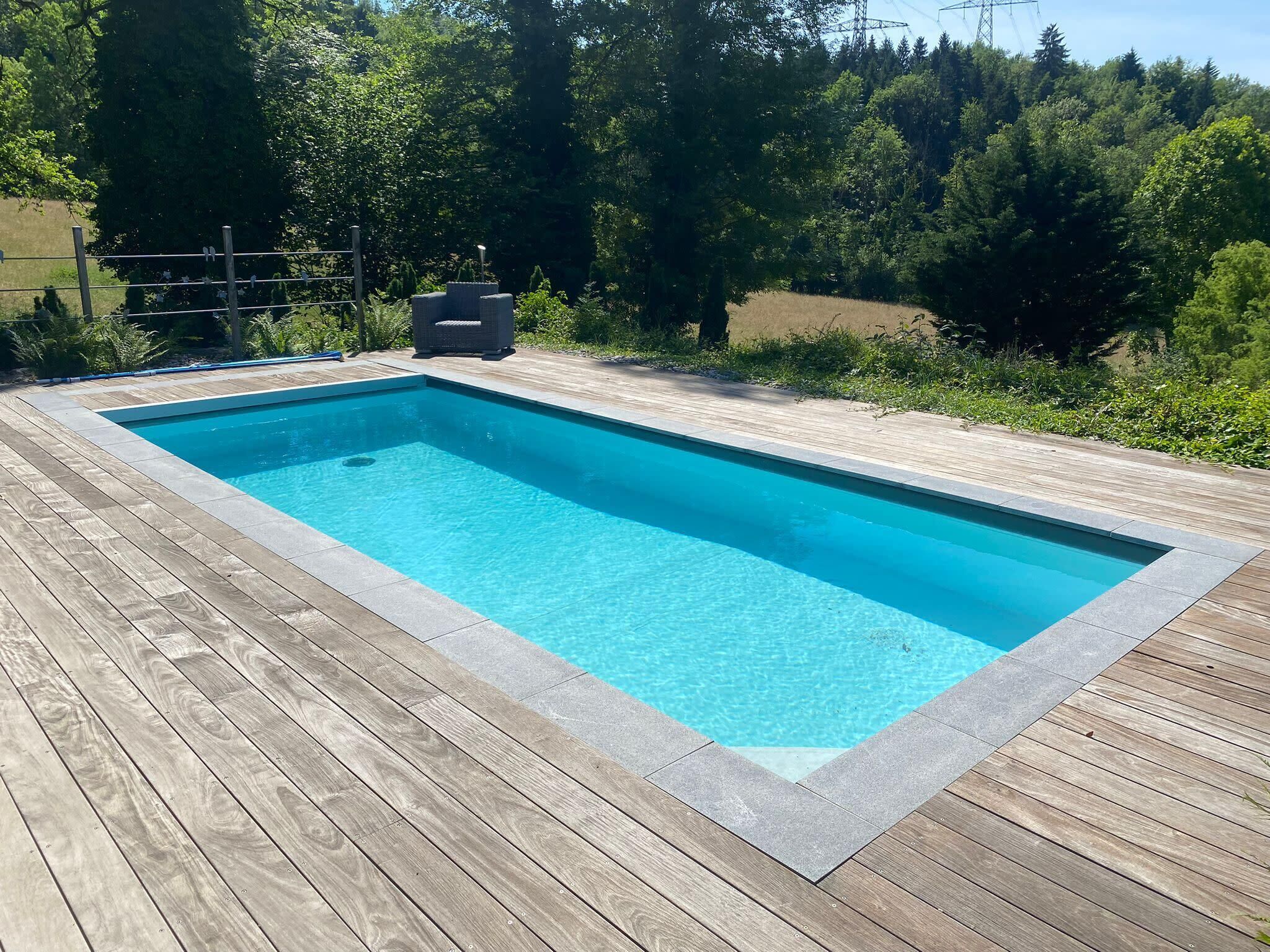 A rectangular swimming pool with a wooden deck surrounding it.