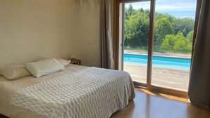 A bedroom with a large bed, a nightstand, and a view of a swimming pool through a sliding glass door. - Beautiful Villa with Pool and Lake View (Attignat-Oncin)