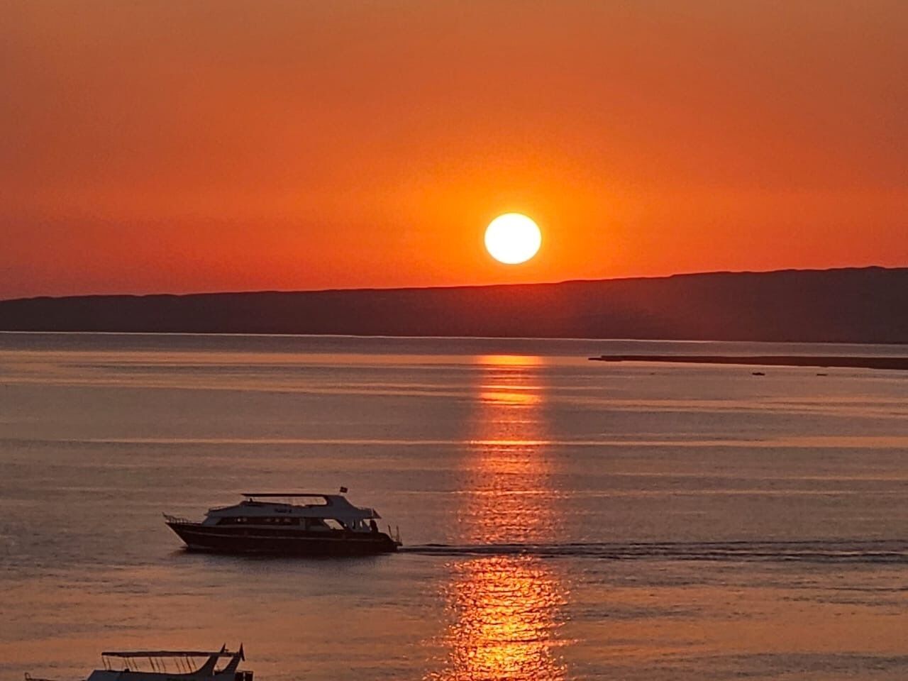 A sunset over a calm body of water with a boat in the foreground.