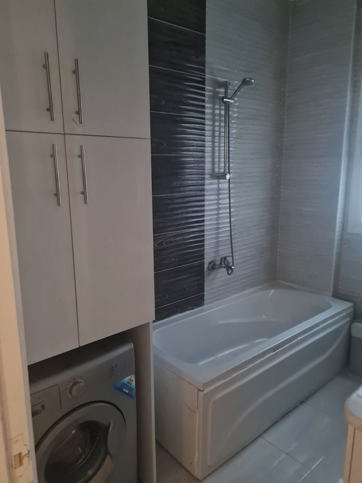 Een badkamer met een bad, een wasmachine en een douchehoek.