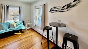 A room with a bed, a small table, a chair, and a decorative wall piece. - Near Huron Lake & downtown  (Port Huron)