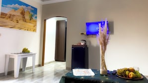 A room with a TV mounted on the wall, a painting of pyramids, a small table with fruits, and a vase with dried plants. - Sneferu Pyramids Golden Gate (Giza)