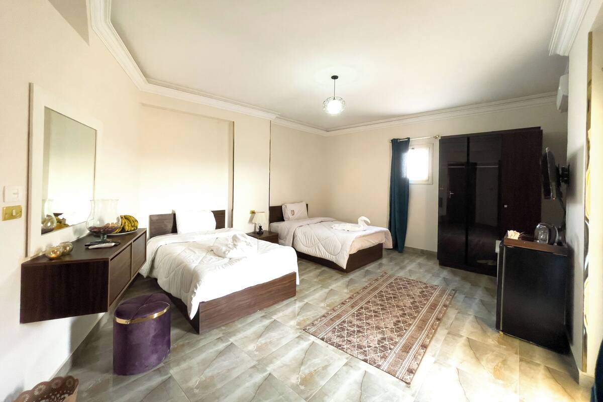 A hotel room with a large bed, a smaller bed, a desk, a wardrobe, and a bathroom.