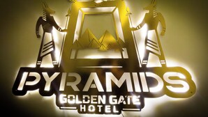 A hotel sign with the name "PYRAMIDS GOLDEN GATE HOTEL" and a graphic of two figures holding a frame with pyramids inside. - Sneferu Pyramids Golden Gate (Giza)