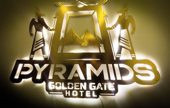 Une enseigne d’hôtel portant le nom « PYRAMIDS GOLDEN GATE HOTEL » et représentant graphiquement deux personnages tenant un cadre contenant des pyramides.