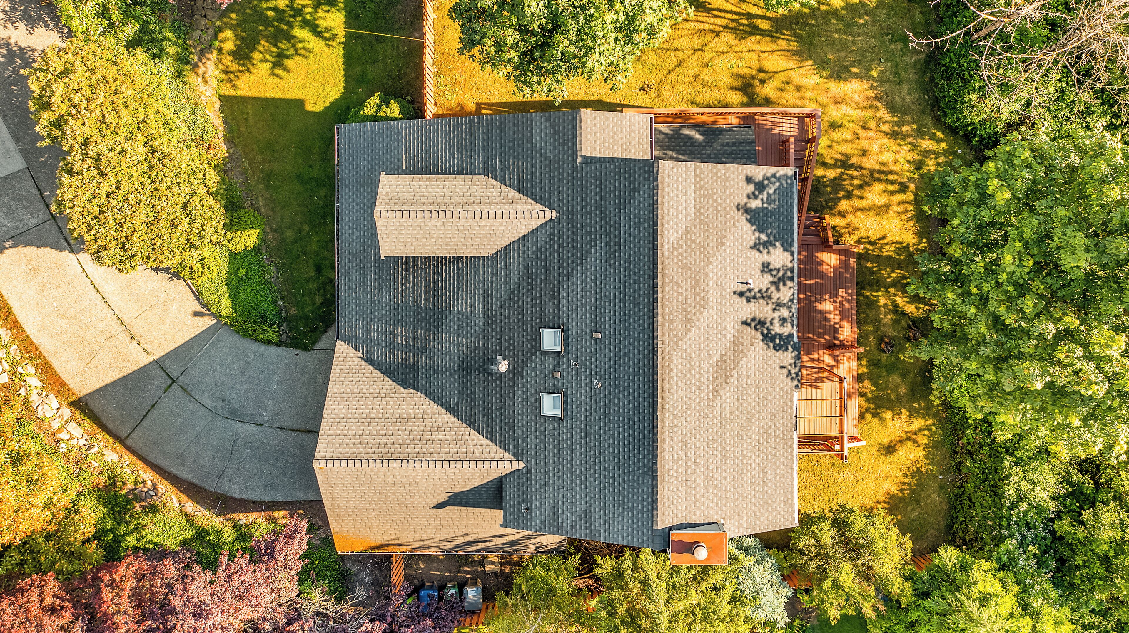 An aerial view of a building with a sloped roof, a fenced area, and surrounding greenery.