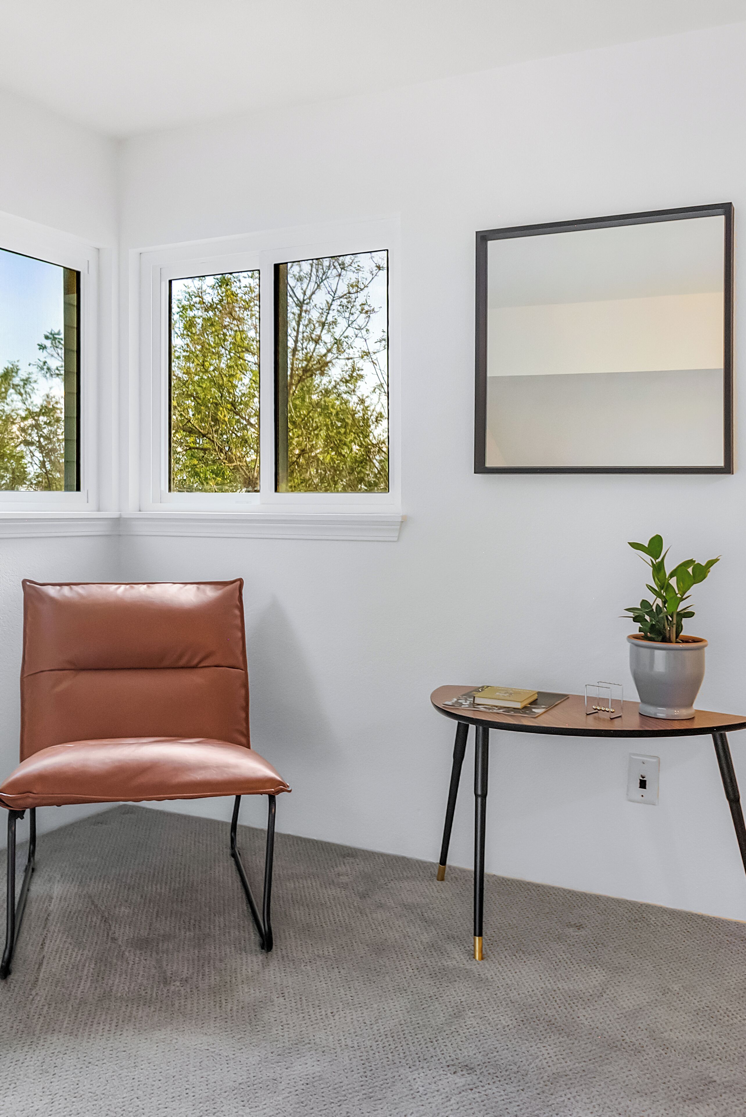 A room with a leather chair, a small table with a plant, and a framed picture on the wall.