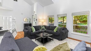 Ein modernes Wohnzimmer mit einem Ecksofa, einem Couchtisch und einem großen Fenster mit Blick auf Grünflächen.