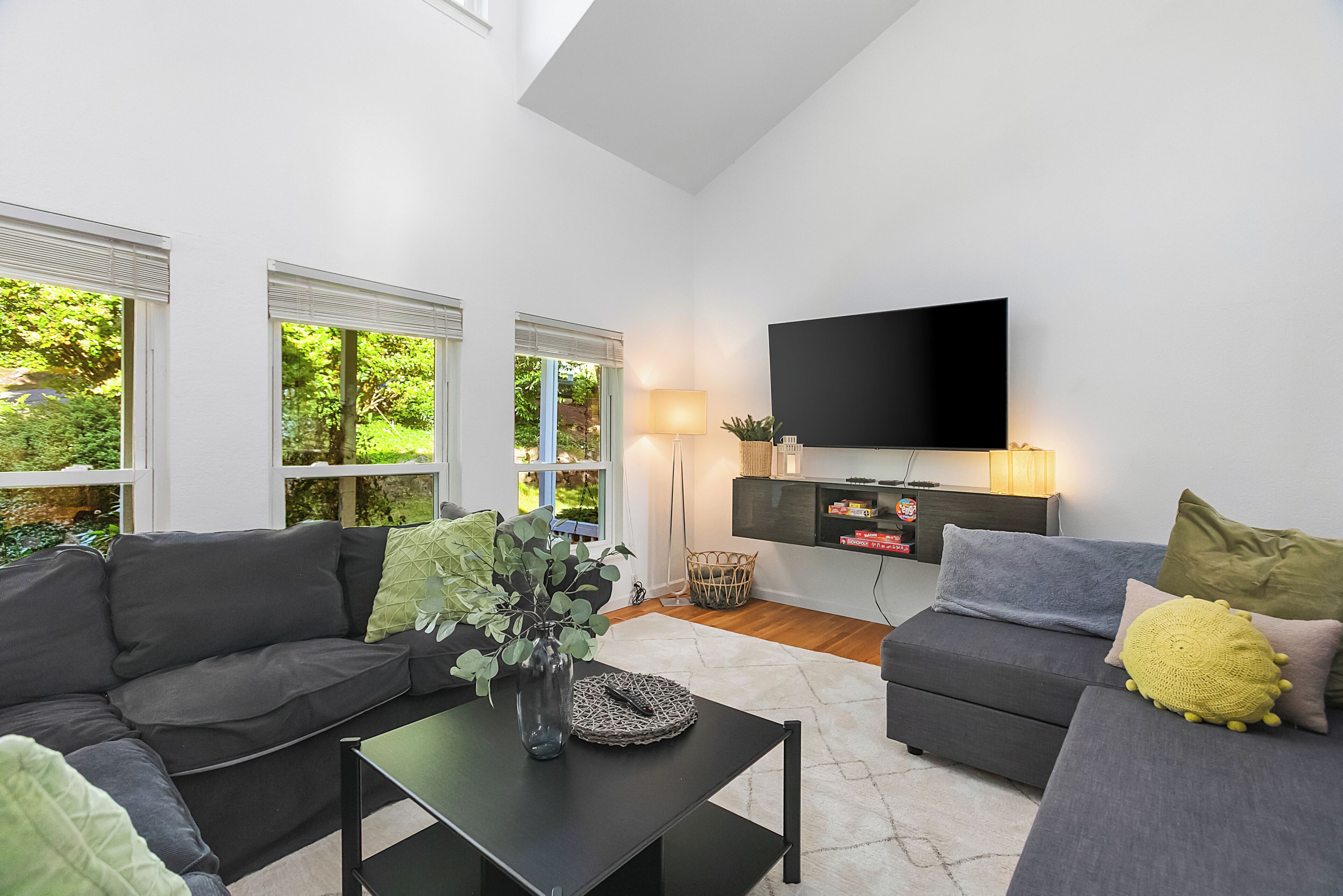 Ein modernes Wohnzimmer mit großem Flachbildfernseher, zwei Sofas, einem Couchtisch und einem großen Fenster mit Jalousien.