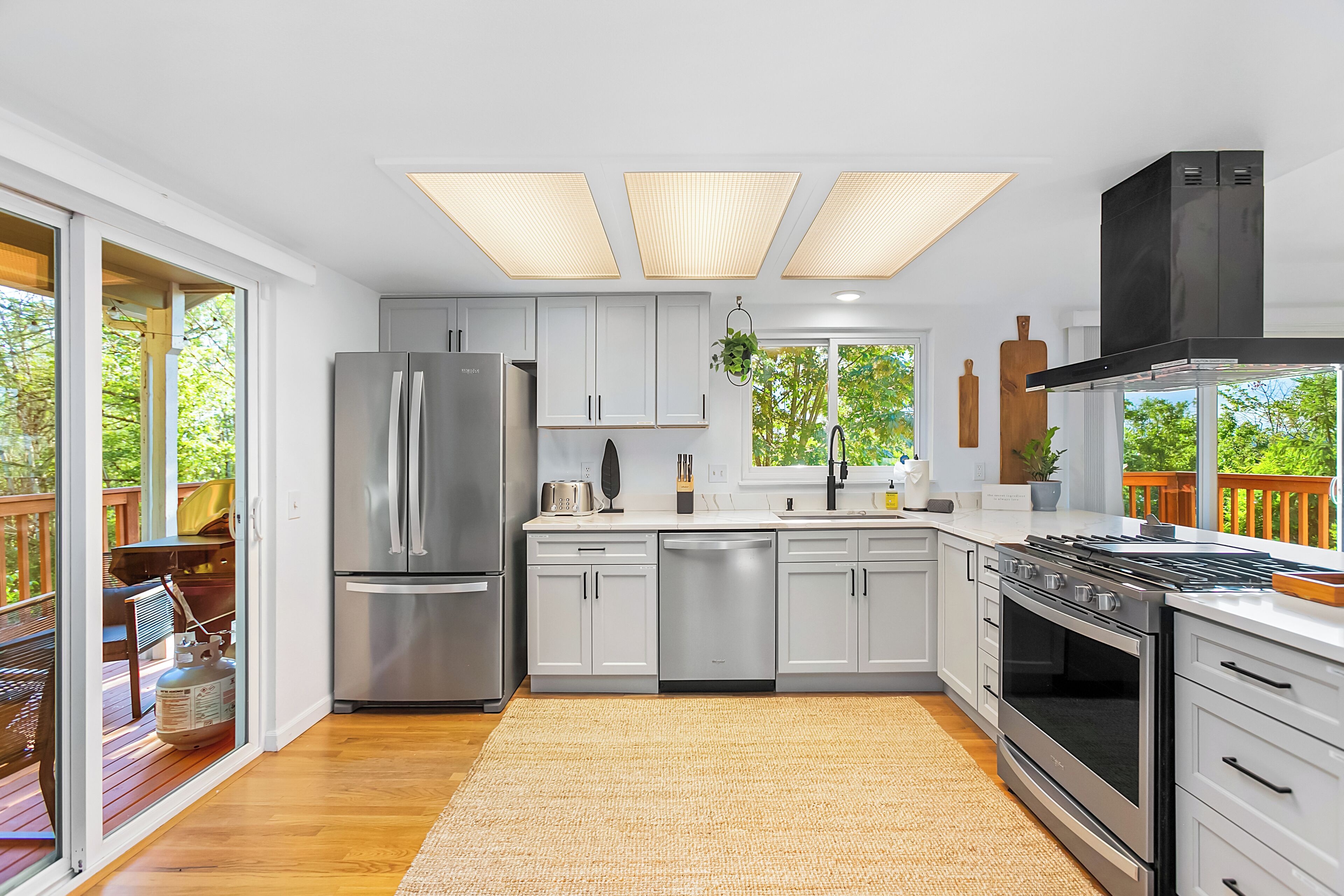 A modern kitchen with stainless steel appliances, white cabinetry, and a large window overlooking a deck.