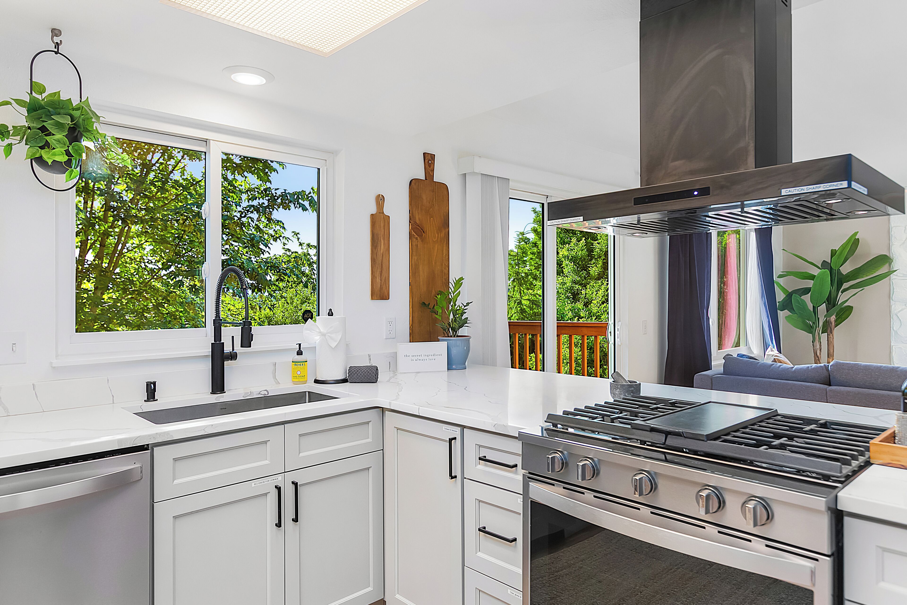 A modern kitchen with white cabinetry, a stainless steel stove, and a large window overlooking greenery.
