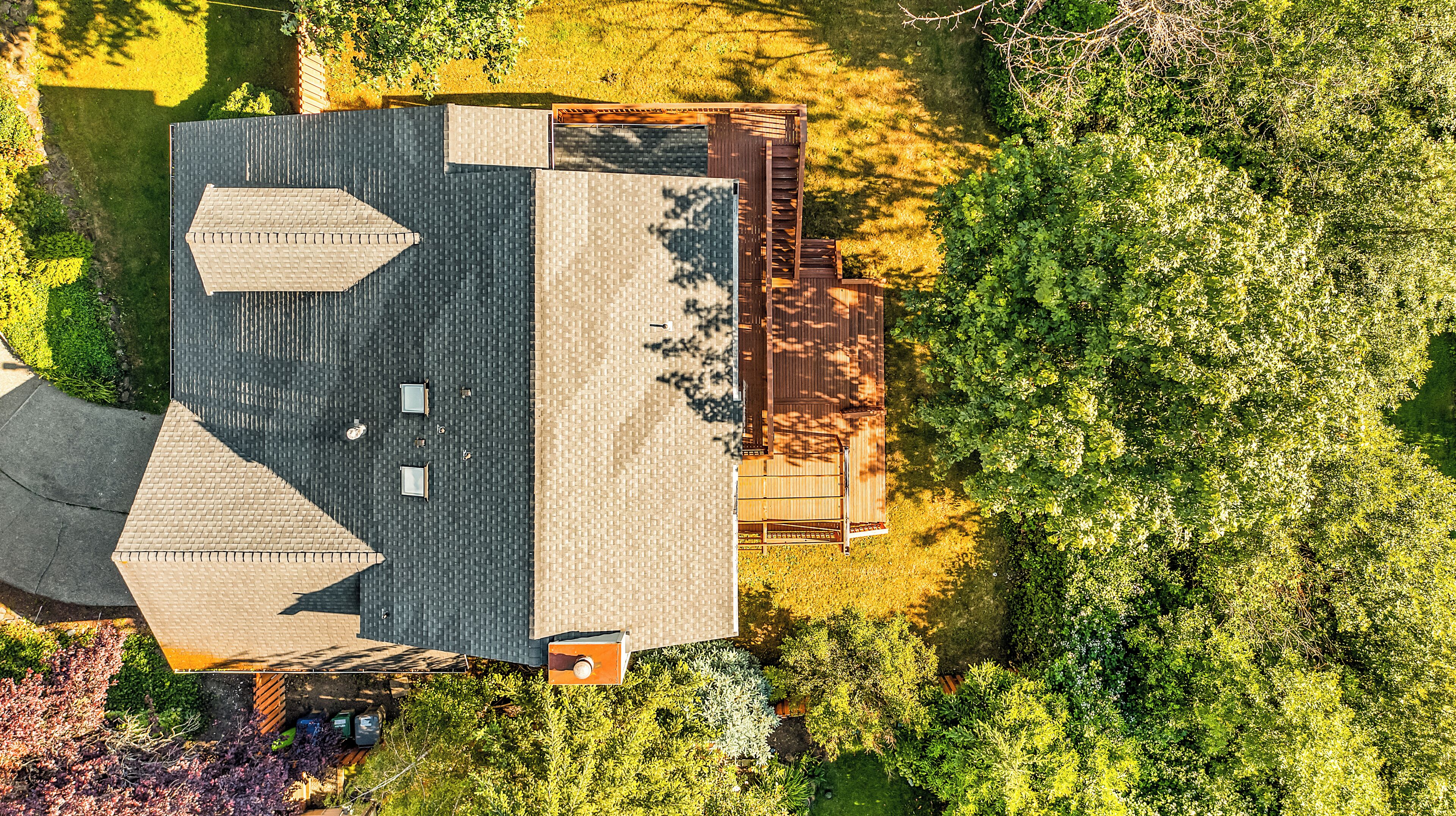 An aerial view of a house with a sloped roof, a fenced yard, and dense surrounding vegetation.