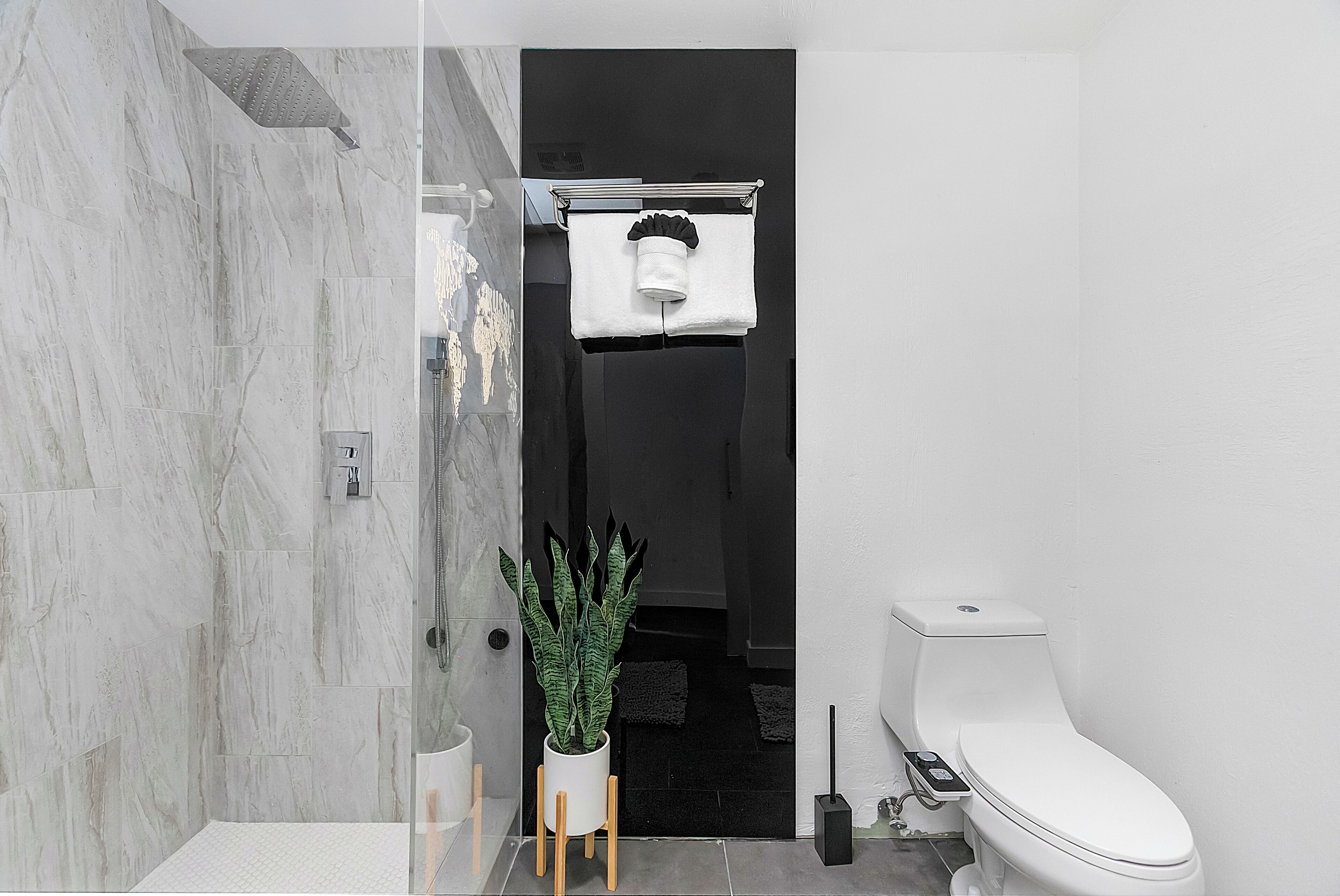 A modern bathroom with a glass shower enclosure, a potted plant, a white toilet, and a towel rack.