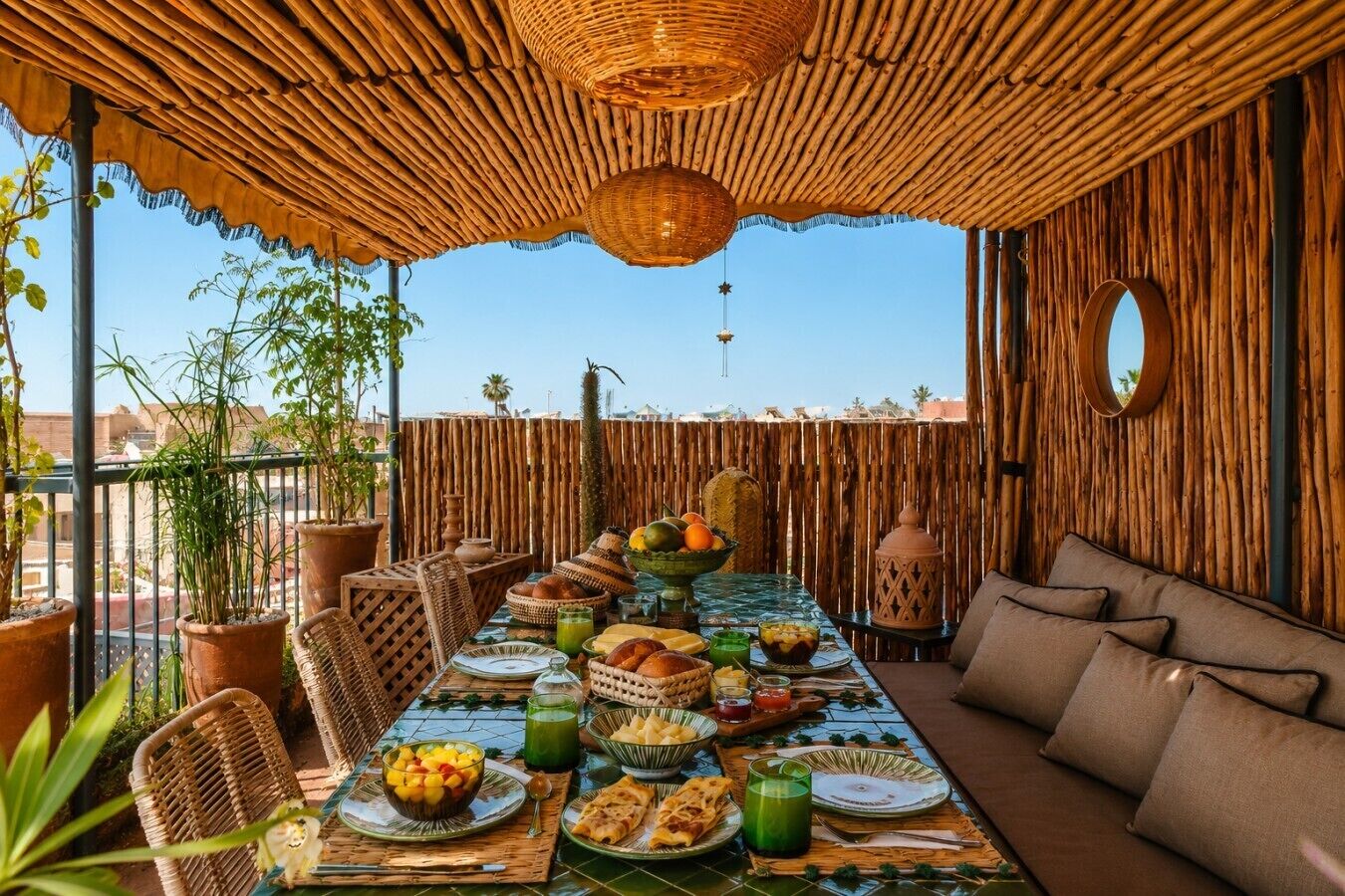 A dining area with a long table set for a meal, surrounded by wicker chairs and a sofa, with a bamboo wall and a clear view of the sky.