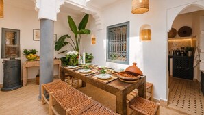 A dining area with a wooden table, wicker chairs, and a large plant. - Riad Belvi - Breakfast - 10mn Jemaa El Fnaa-Pool (Marrakech)