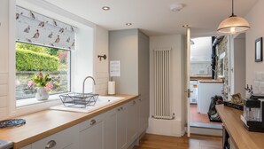 Une cuisine moderne avec un plan de travail en bois, un évier, une fenêtre donnant sur un espace verdoyant et un radiateur.