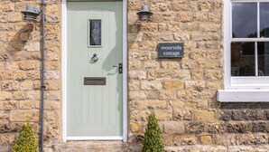 Une petite maison en pierre avec une porte verte, une petite fenêtre et une pancarte indiquant « Moorside Cottage ».