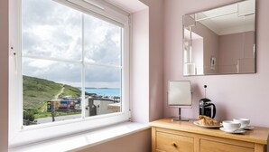 Een kamer met een groot raam, een houten dressoir, een spiegel en een koffiezetapparaat.