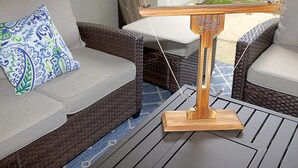 Ein Korbusofa mit gemustertem Kissen, ein Holztisch mit Metallgestell und ein kleiner Holzständer mit Text.