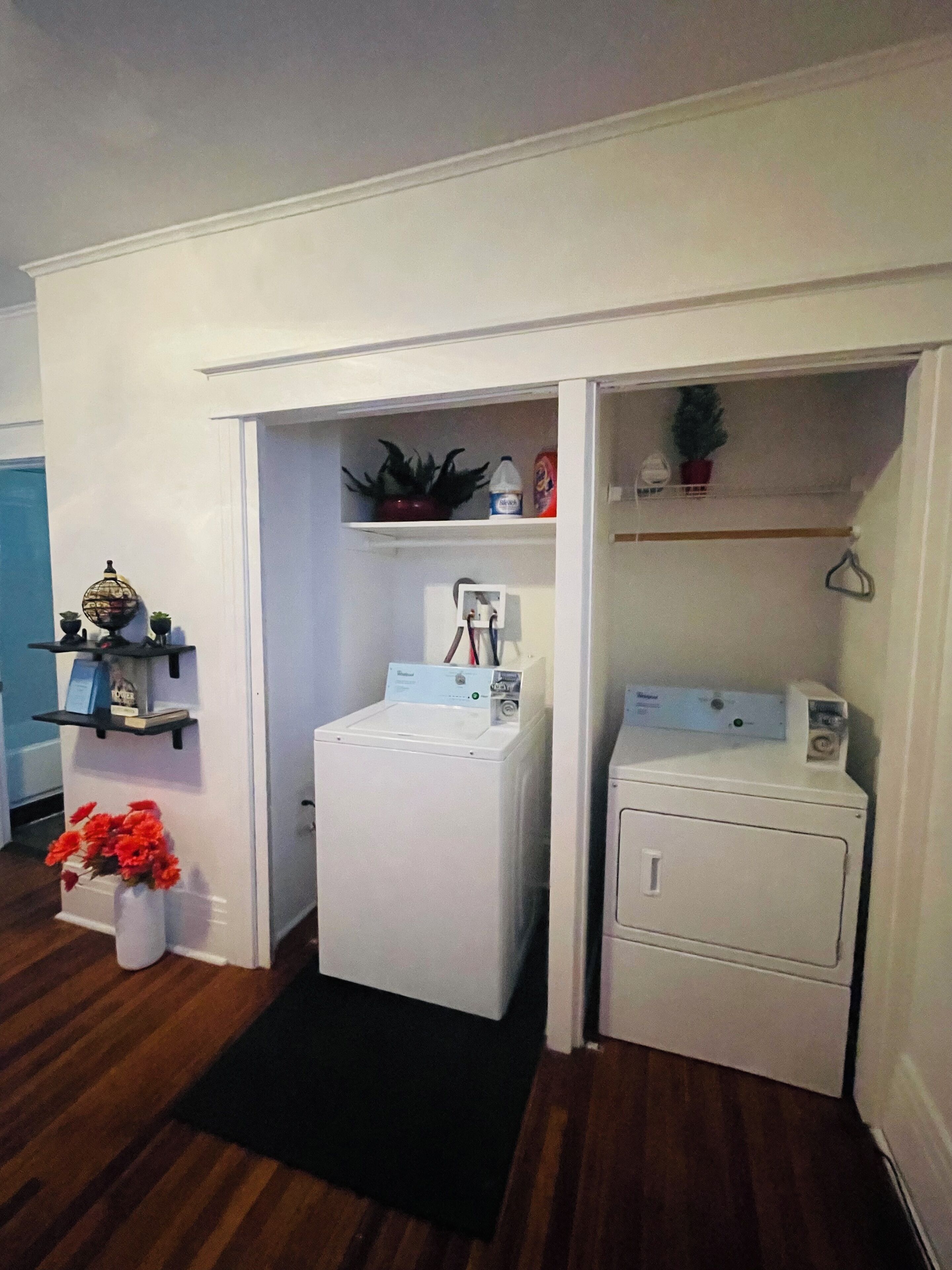 Une buanderie avec deux machines à laver blanches, une étagère ornée d’objets décoratifs et une petite plante en pot.
