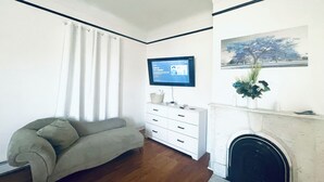 Una sala de estar con un sofá, un televisor montado en la pared, una chimenea y un cuadro.