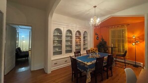 Un comedor con mantel azul, sillas de madera, candelabro y un armario blanco con puertas de cristal.
