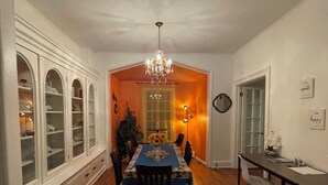 Comedor con candelabro, una mesa con mantel floral y un aparador con puertas de vidrio.