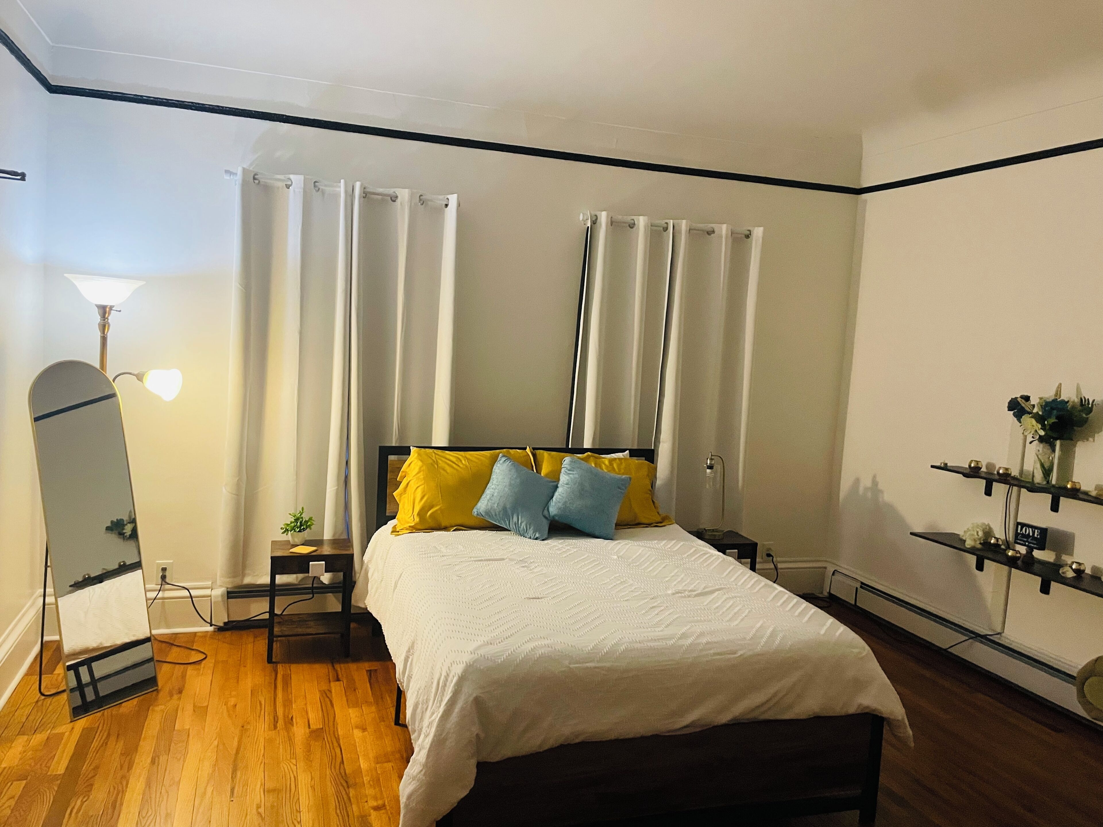 Une chambre à coucher comprenant un lit, une table de chevet, un miroir, une lampe et une étagère avec des objets décoratifs.
