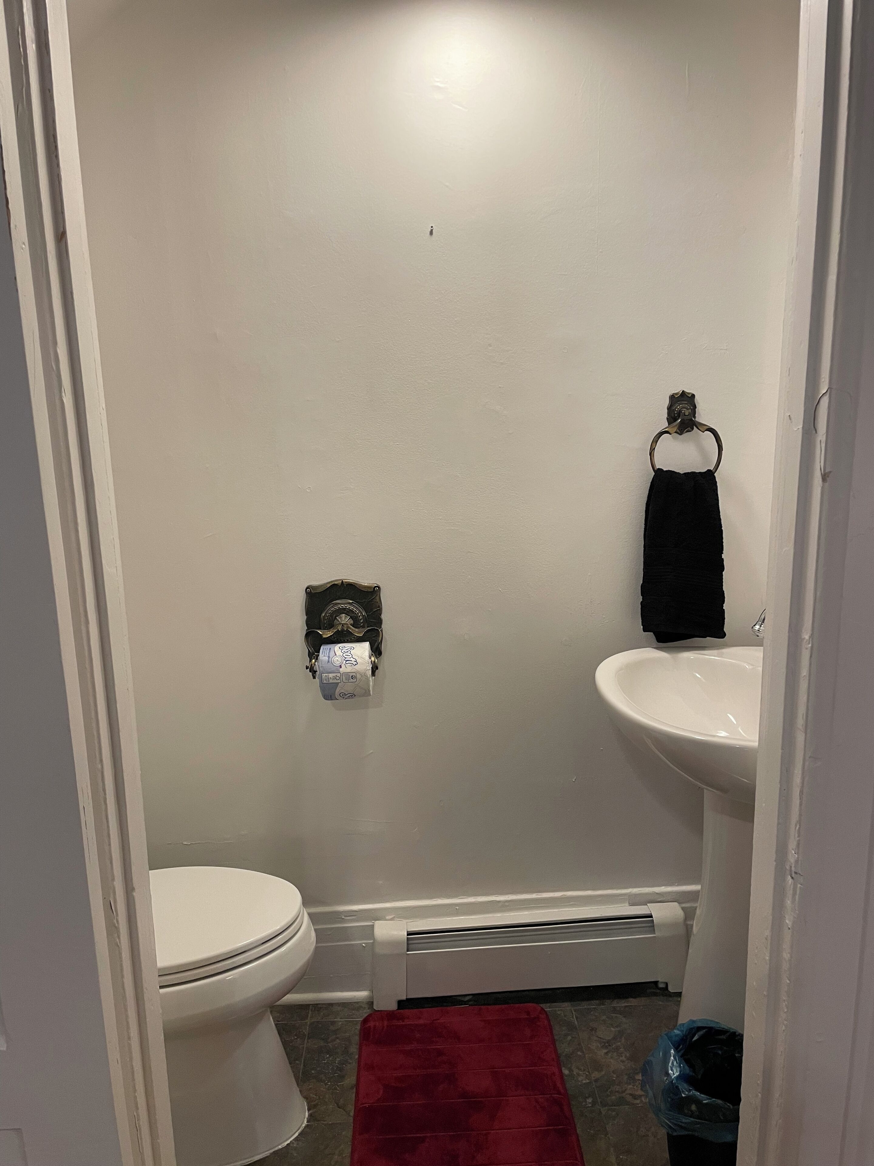 A bathroom with a toilet, sink, towel rack, and a wall-mounted toilet paper dispenser.