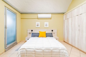 A bedroom with a bed, a wardrobe, a door, and an air conditioning unit.