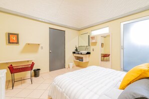 A hotel room with a bed, a bedside table, a mirror, a small window, and a door.