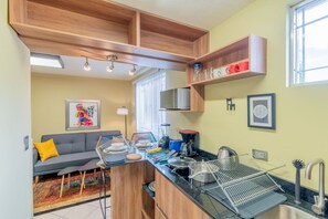 A compact kitchen with wooden cabinetry, a microwave, and a sink. There is a dining area with a sofa and a colorful artwork on the wall.