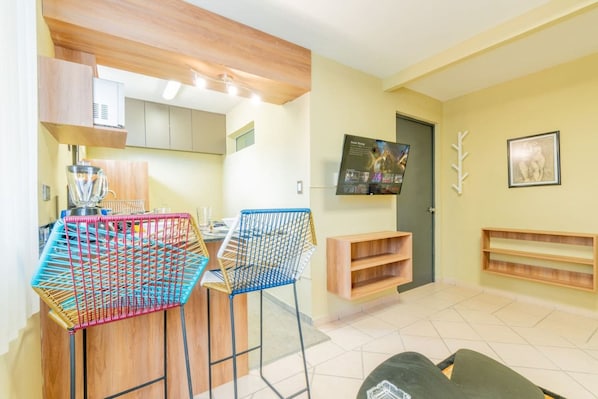 A modern kitchen with a dining area, a television mounted on the wall, and a wooden cabinet.