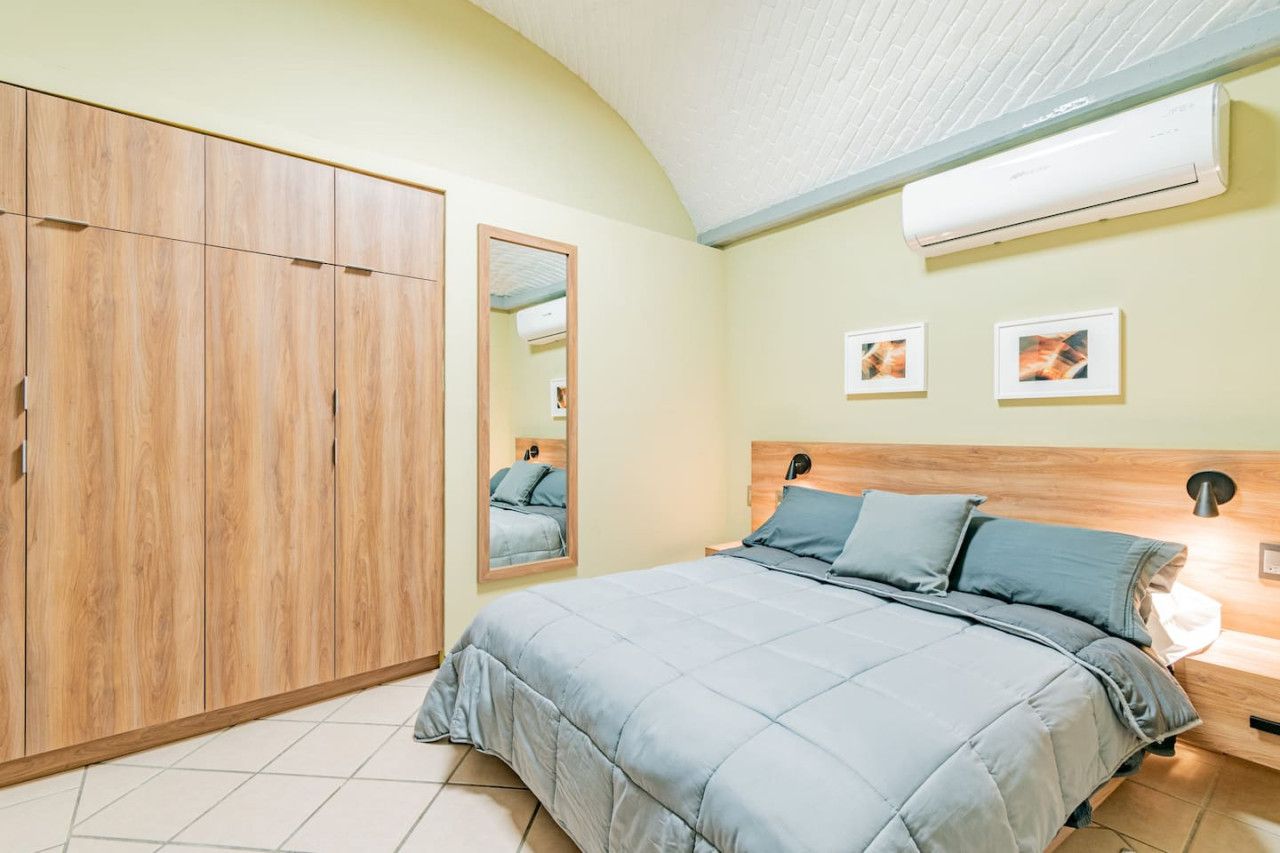 A bedroom with a bed, a wardrobe, a mirror, and an air conditioning unit.