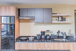 A modern kitchen with built-in appliances, a countertop with various kitchenware, and a visible dining area with a chair.