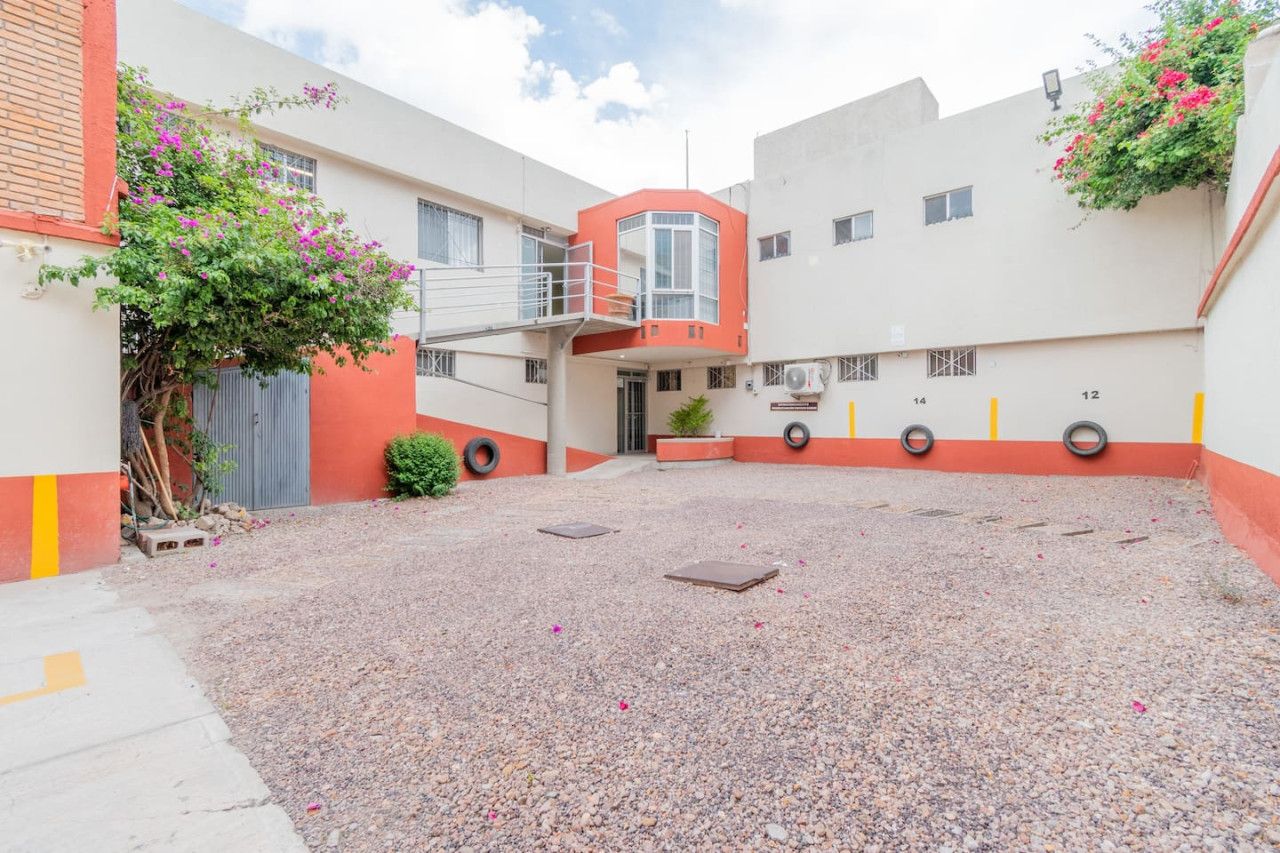 A courtyard with a building featuring a red and white facade, a small balcony, and a gravel ground.