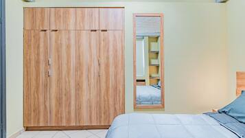 A bedroom with a large wardrobe, a bed with a blue bedspread, and a mirror on the wall.