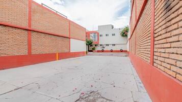 An outdoor courtyard with brick walls, a concrete floor, and a building in the background.