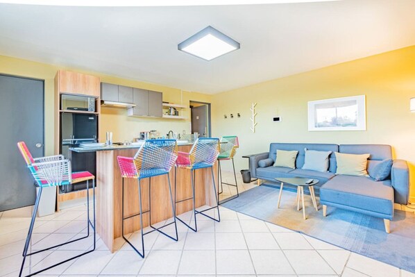 A modern kitchen with a central island, bar stools, a sofa, and a small table.