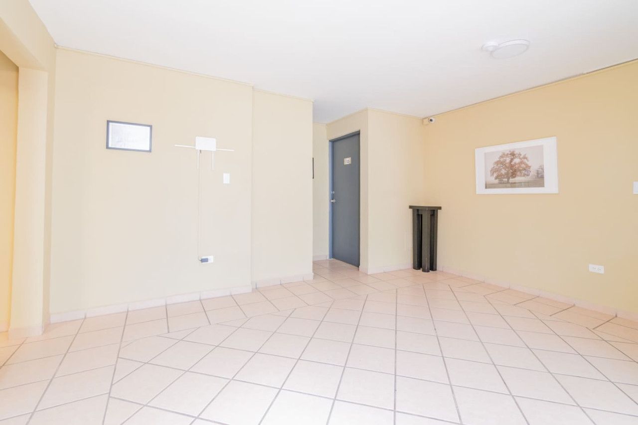 A spacious room with a tiled floor, a door, a small trash bin, and a framed picture on the wall.